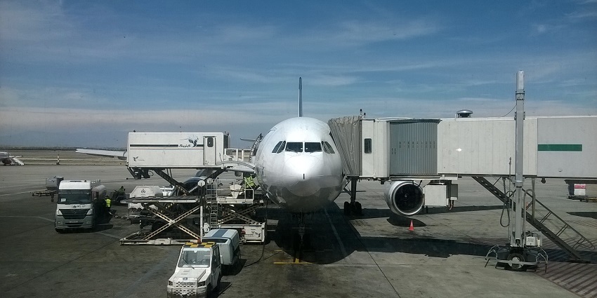 Airbus parked at an airport with cargo loading and unloading with several vehicles parked below.