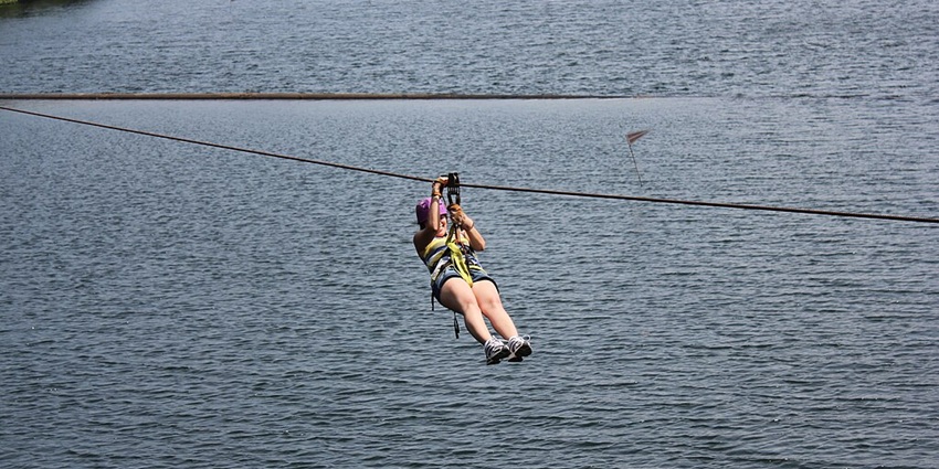 Person smiling while ziplining, holding the hook over a large waterbody and greenery