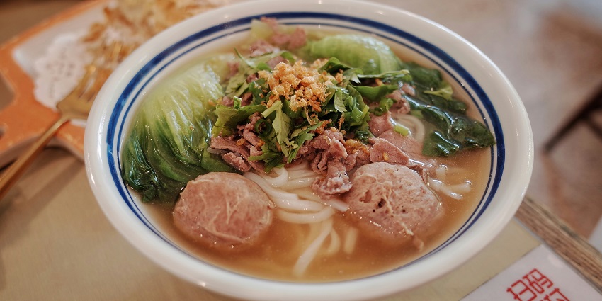 Image of a bowl of rice noodles with veggies and meat served on a nice bowl
