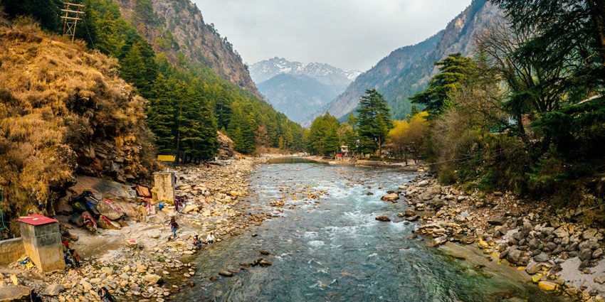 An image of the Kheerganga Trek, with a narrow rocky path, green valley, and snow-capped mountains.