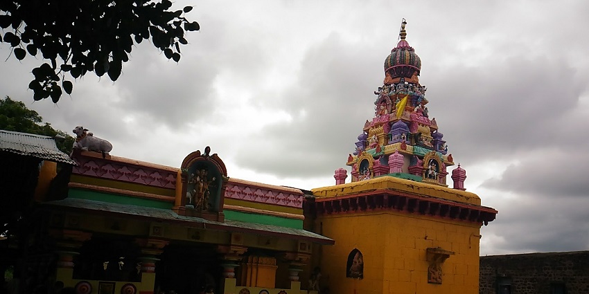 Brightly painted Khol Khandoba Mandir with a tiered tower, under an overcast sky.