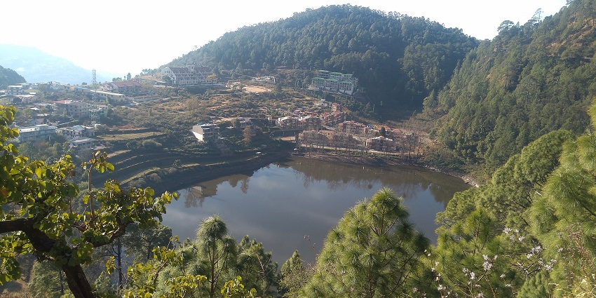 Khurpatal lake with a small water body surrounded by green mountains and buildings