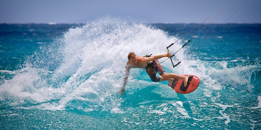 A man kite surfing, onboard an orange surfboard, one of the Morjim Beach water sports.