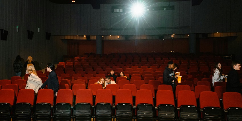 An image of a movie theatre with an audience watching a film showing a close-up of sneakers.