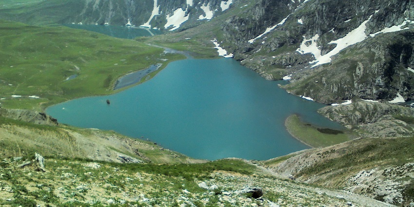 Krishansar lake with a small, clear water body surrounded by green shorelines and white snow