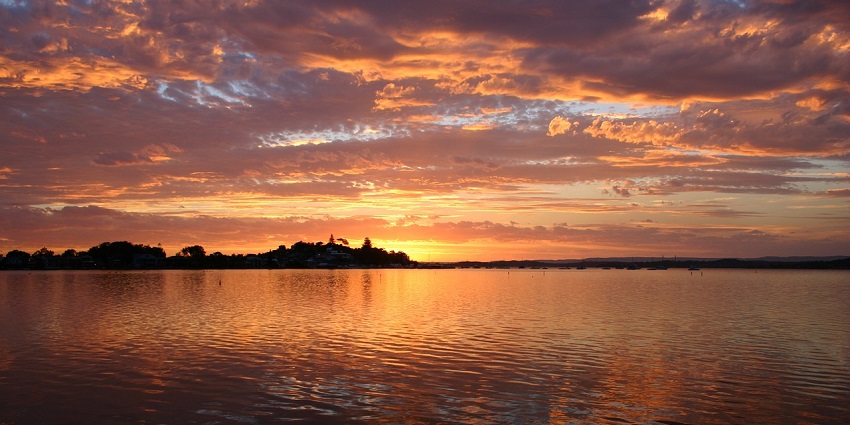 A tranquil lake at sunset, with a silhouetted tree and vibrant colors reflecting on the water.