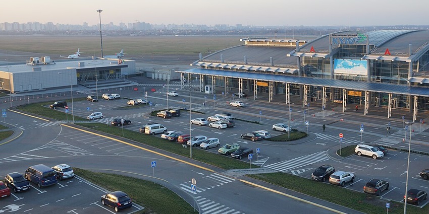 Panoramic view of Kyiv International Airport (Zhuliany) with a lot of parked cars, terminal, and runway with aircraft