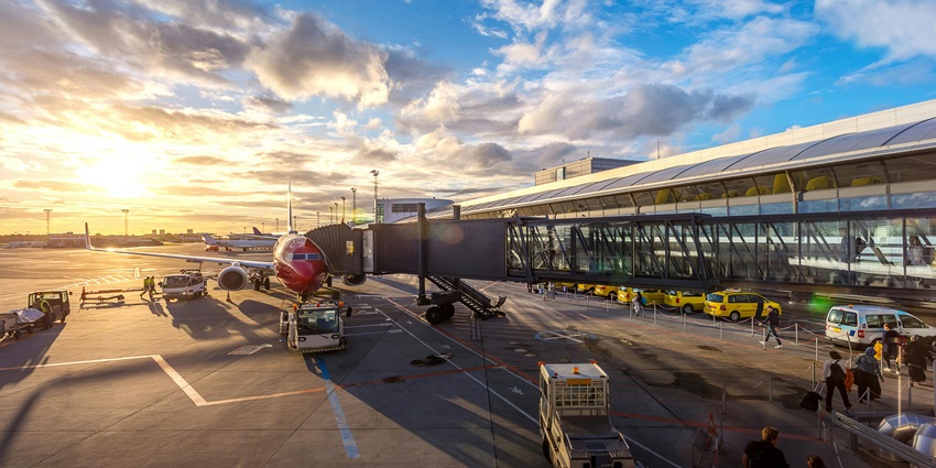 Passengers boarding an airplane via jet bridge at a modern airport terminal during sunset