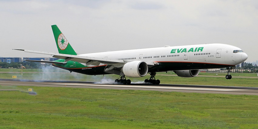 Green and white commercial aeroplane landing on a runway with signages and grass