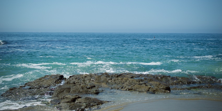 Scenic coastline with rocky cliffs, sandy beach, and waves crashing against the shore