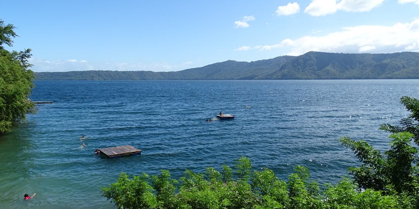 Laguna de Apoyo’s blue waters reflect the sky, surrounded by lush green hills.