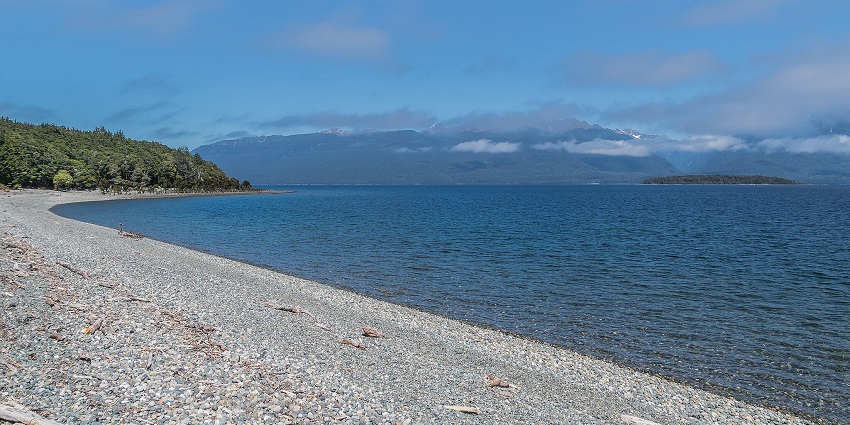 An image of Lake Te Anau, reflecting a blue sky, framed by snow-capped mountains.