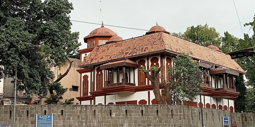 Lal Mahal behind a wall with its red and white brick architecture surrounded by trees.