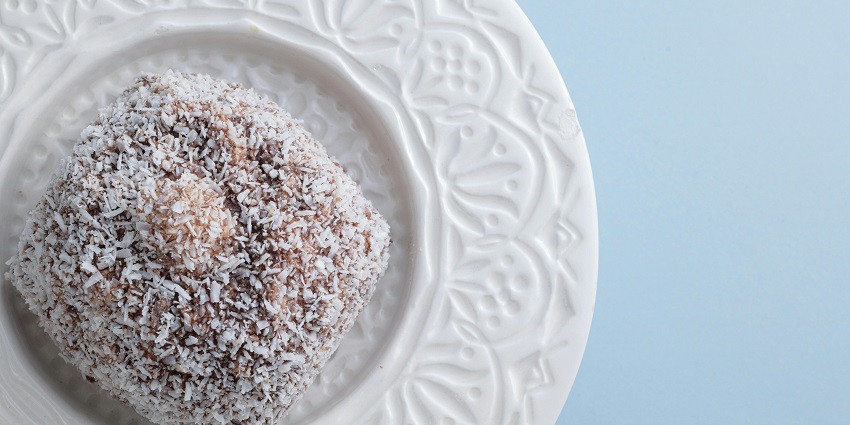 A single lamington with crushed coconut powder served in a white, unique design plate