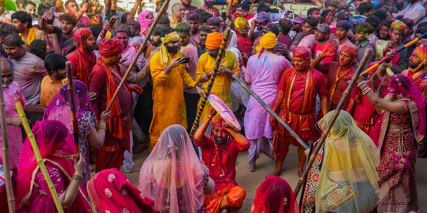 An image of the Lathmar Holi festival, one of the most unique festivals in India, with women hitting men with sticks while men use shields.