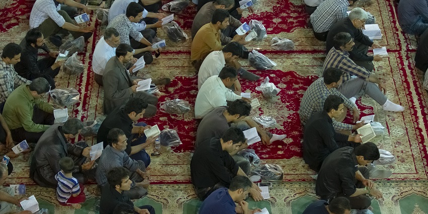 An image showing a woman holding prayer beads and a holy book while praying on Laylat al Qadr.