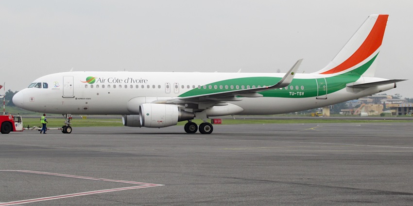 Green, red and white aeroplane parked on the runway of an airport with a man standing