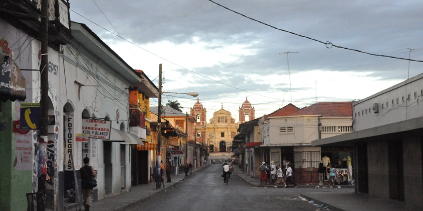 A street in León, Nicaragua, is lined with colonial-style buildings and a few parked vehicles.