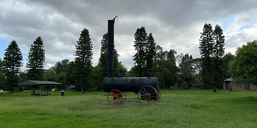 Lighthorse park’s green land area and trees with a replica of a steam engine for display