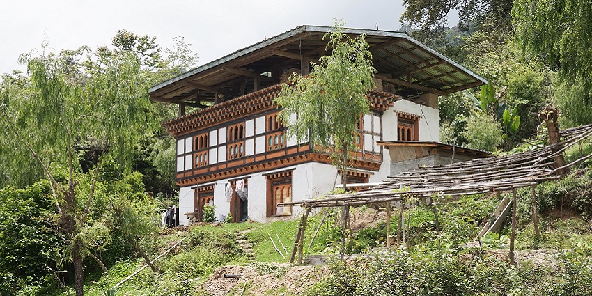 An image of a traditional Bhutanese house on a hill, wooden carvings, surrounded by trees