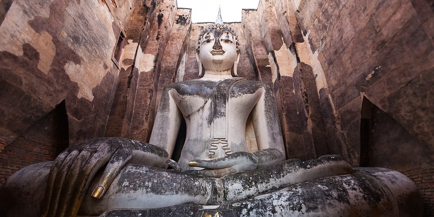 A massive seated Buddha peeks through an ancient stone arch at Wat Si Chum, Sukhothai Historical Park.