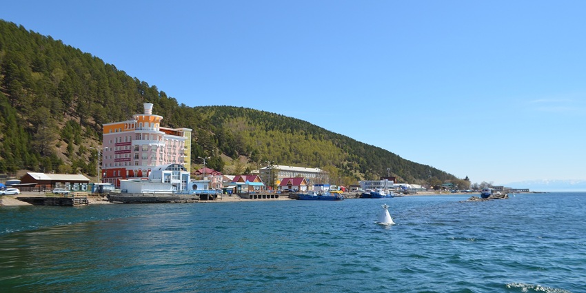Listvyanka with vibrant multiple buildings, sandy shoreline and green mountains.