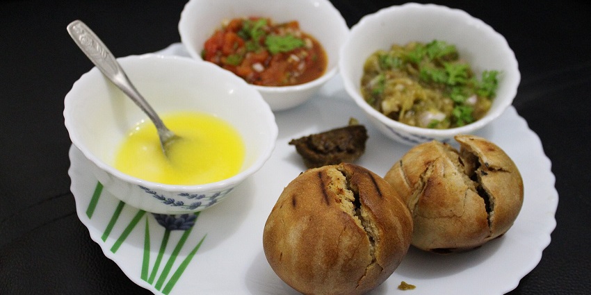An image of Litti Chokha, stuffed bread buns with creamy white sauce, garnished with herbs, and other vegetable dishes on the table