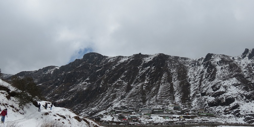 People walking on the snow-covered trails and Changu Lake below with snowy mountains