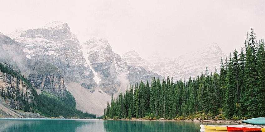 Moraine Lake with colourful boats on the right side, a shoreline, trees and mountains