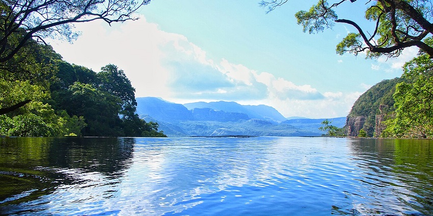 Clear blue water with reflections, framed by trees, facing Knuckles Mountain Range views.