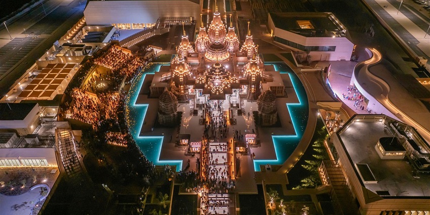 Aerial night view of a grand BAPS Hindu Mandir, Abu Dhabi, illuminated with golden lights