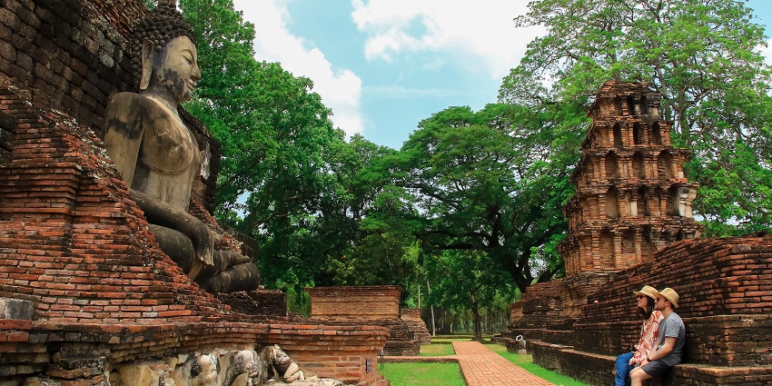 Sightseers gazing at a majestic seated Buddha statue at Sukhothai Historical Park’s ancient site.
