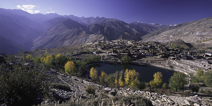 Nako Lake surrounded by rocky shorelines, tall trees and the nako village at a distance