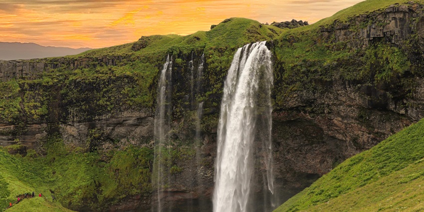 An image of a cascading waterfall surrounded by mountains and water, like McLean Falls.