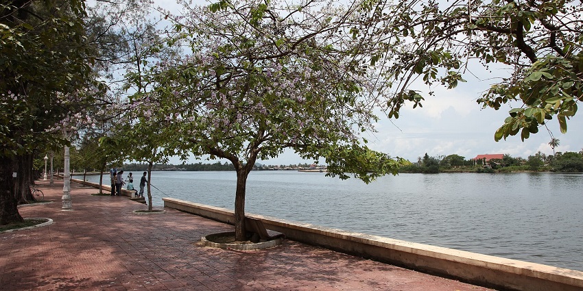 Image of Riverside Street in Kampot, Cambodia, with buildings, vehicles, and a river view