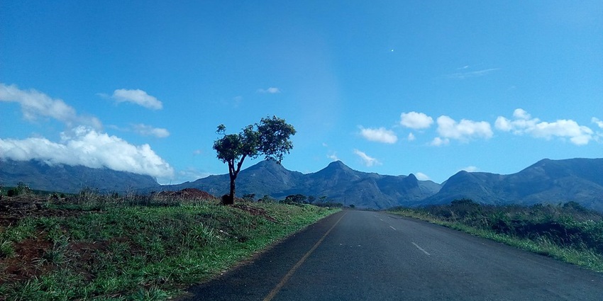 A road in Mozambique with distant green mountains and surrounded by green plains