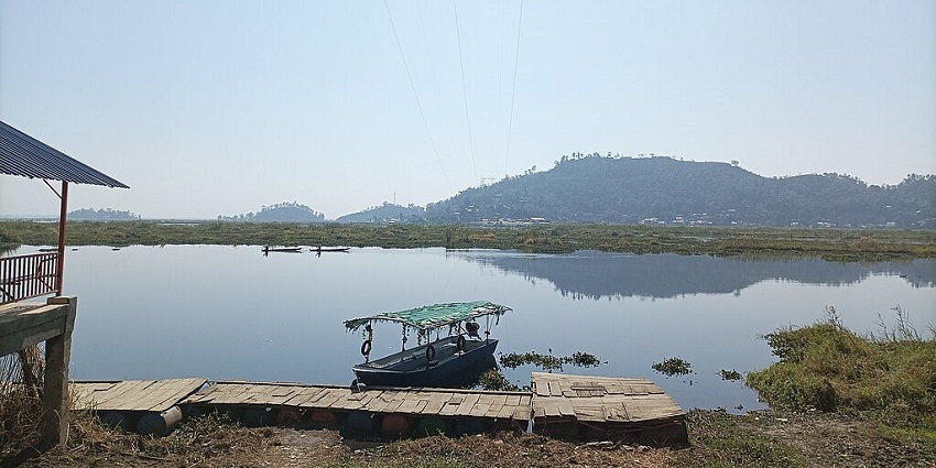 Landscape of the floating lake in Manipur with wooden ferry, boat parked, distant green shoreline and hills.