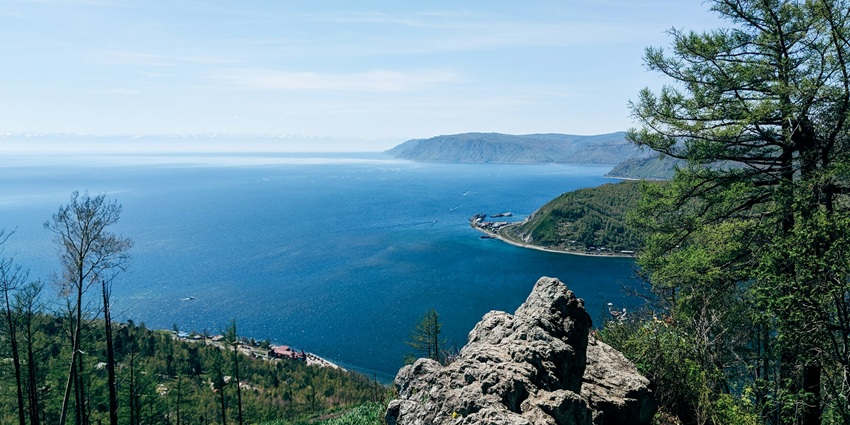 Baikal Lake from the top with a large water body, green shores and distant green mountains.