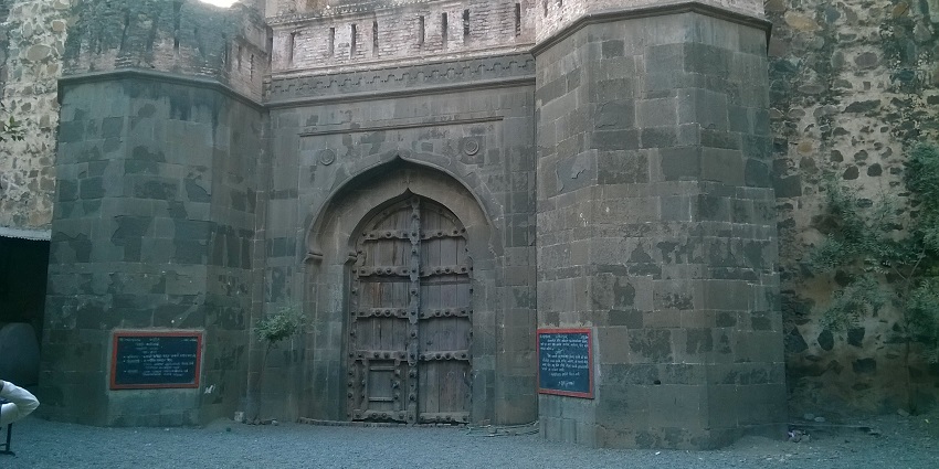 An image of the big wooden entrance doors of the historical Malegaon Fort with sign boards