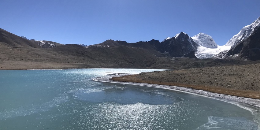 Clear sky and surrounding mountains, reflected in the water of Gurudongmar Lake in March