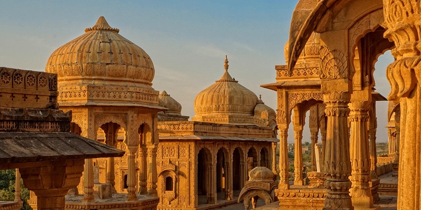 Temple building with a golden dome at sunset, surrounded by trees and warm light.