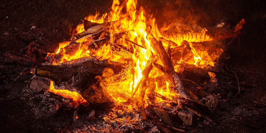 An image of an intense fire with vivid orange and yellow flames, engulfing and charring wooden logs, lit during the Lohri festival.