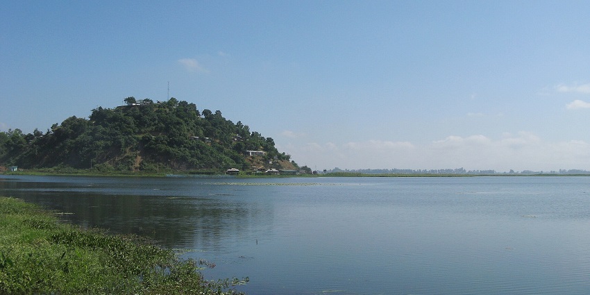 Loktak Lake with water weeds on the large water body and distant buildings hidden in the hill