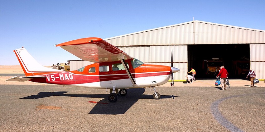 A small aircraft parked on the tarmac in Lüderitz, Namibia, with people entering the shed