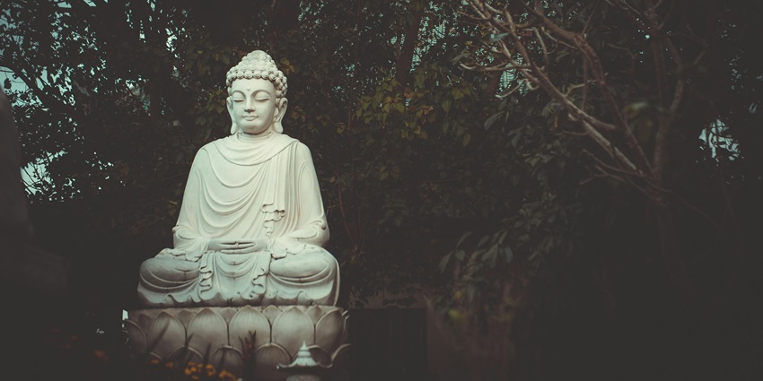 White Buddha statue in meditation pose, surrounded by trees in a peaceful outdoor setting