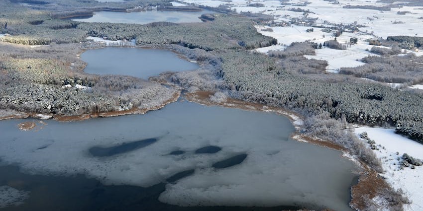 View of a water body with intricate ice patterns amid snow-covered forests and mountains.