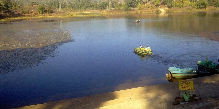 Lake with a small greenish water body, multiple boats in the lake with people and hills