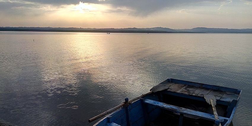 Vast lake with distant mountains and lush greenery under a partly cloudy sky in Kangra.