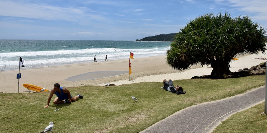 Visitors relaxing on Main Beach with golden sands and turquoise waves under a clear blue sky.