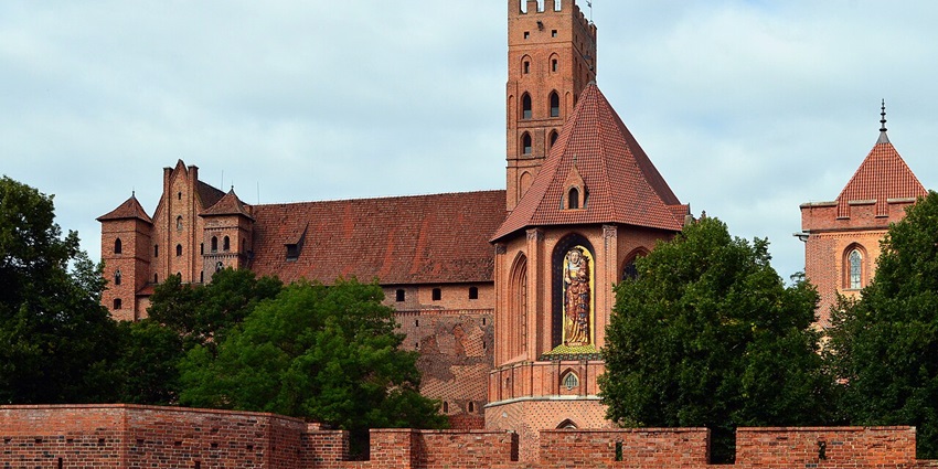 Panoramic view of Malbork Castle's red-brick walls and defensive towers.